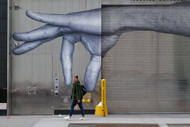 a woman walks in front of a mural of a hand pinching